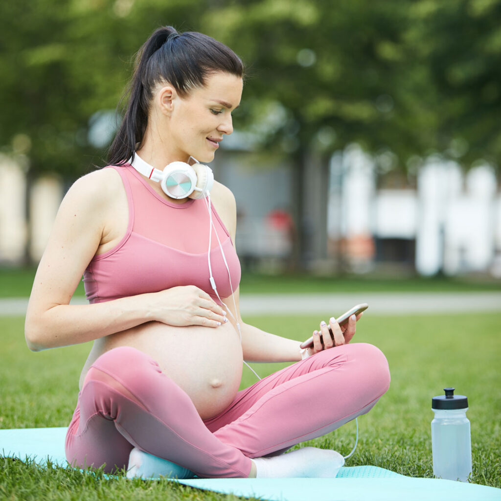 een fitte zwangere vrouw zit in het park